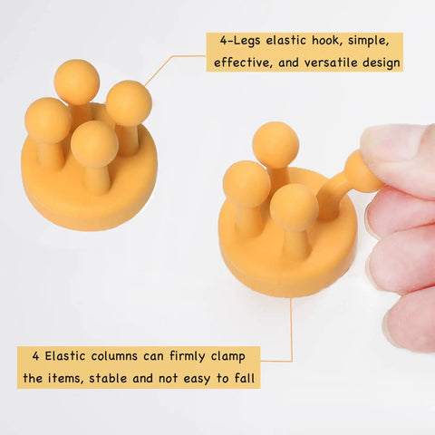 Close-up of orange Four Pack Self Adhesive Silicone Toothbrush Holders Wall Mounted Mirror Hooks with elastic legs, held by hand.