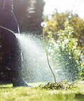 Person using 2-Gallon Pump Sprayer For Weeds With Rust-Proof Dent-Proof Poly Tank, spraying on lawn with sunlight.