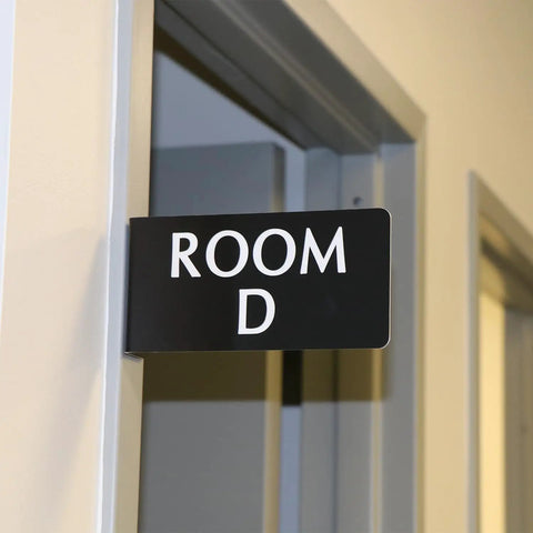 Heavy Duty Horizontal Warehouse Aisle Signs Custom Engraved L Shaped Rack Markers With Kickass Durable ABS Plastic Build Pre Drilled Mounting Holes Ready To Hang Made In Usa hanging on a door indicating Room D.