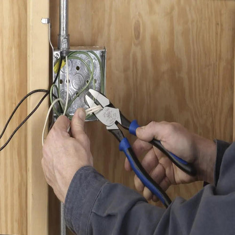 Man using Tough As Nails High Leverage Nine Inch Lineman Pliers to cut wire near an electrical box on wood panel.
