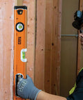935L 24-Inch Magnetic Bubble Level with Adjustable Vial used by worker for wood alignment, high visibility orange, rubberized end caps