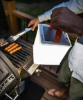 Person using 2 In 1 Solar Camping Lantern And Phone Charger With 300 Lumens Of Bright LED Light near grill at night