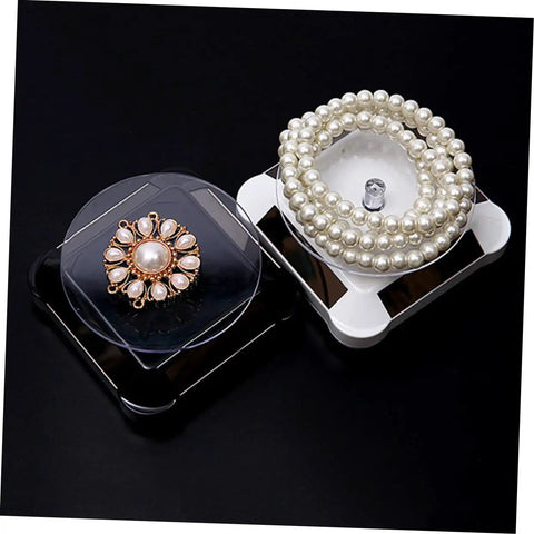 Solar Powered Rotating Jewelry Display Stand With Built In Kickstand showing a pearl bracelet and decorative brooch.