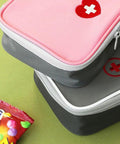 Pink Mini Outdoor First Aid Kit Bag For Travel and Everyday Use with zippers and heart cross symbol on top of a gray bag