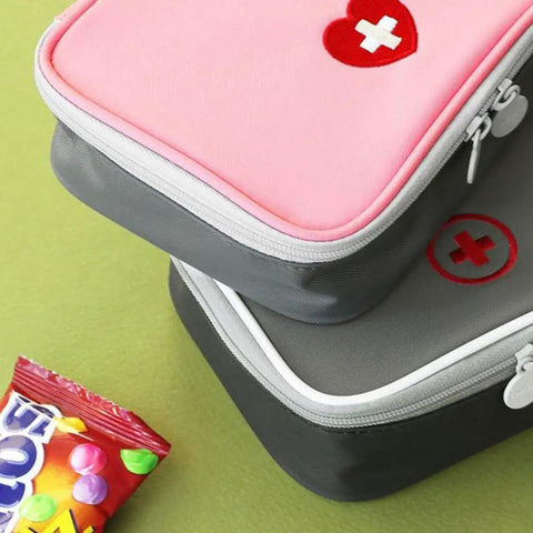 Pink Mini Outdoor First Aid Kit Bag For Travel and Everyday Use with zippers and heart cross symbol on top of a gray bag