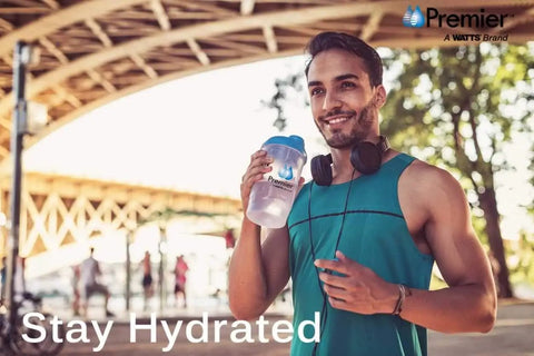 Man holding Premier water bottle under bridge, wearing headphones and tank top, text reading 'Stay Hydrated'. Outdoor fitness scene.