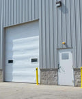 Heavy Duty Beefy Steel Safety Barrier Bollard And Industrial Traffic Control Post With Rock Solid Bright Yellow Finish And Concrete Fillable Base Plate For Warehouse Machine Guard At 42 Inches beside loading dock door.