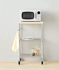 Metal wire kitchen cart with microwave, plates, and jars, on wheels, against a white wall.