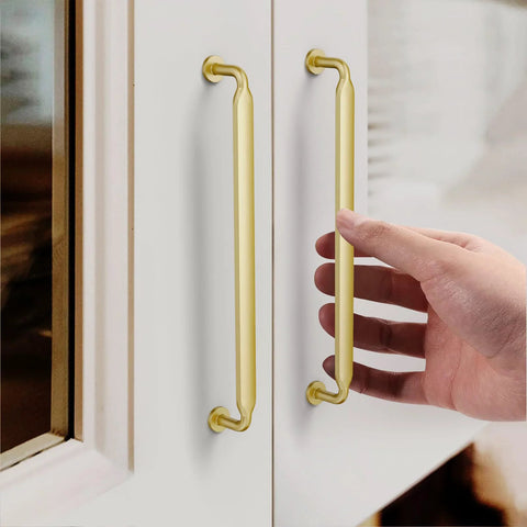 Hand touching Gold Cabinet Pulls 7.5 Inch 10 Pack Zinc Alloy Handles for kitchen cabinets with satin gold finish installed on white cabinet doors.