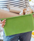 Person holding a green storage bin with paper, showcasing use of 6 Pack Stick-On Adhesive Mini Swivel Caster Wheels For Furniture And Appliances