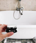 Universal Bathtub Drain Stopper Press Plug with Copper Core held above a white bathtub with chrome faucet.