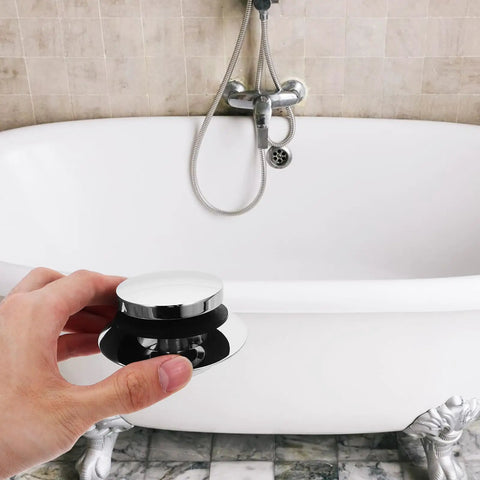 Universal Bathtub Drain Stopper Press Plug with Copper Core held above a white bathtub with chrome faucet.