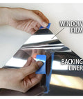 Hands peeling Very Dark Daytime Privacy Window Film With Heat Control Mirror Silver Tint Extra Reflective Silver Shade 36 Inch by 12 Foot Roll from backing liner.