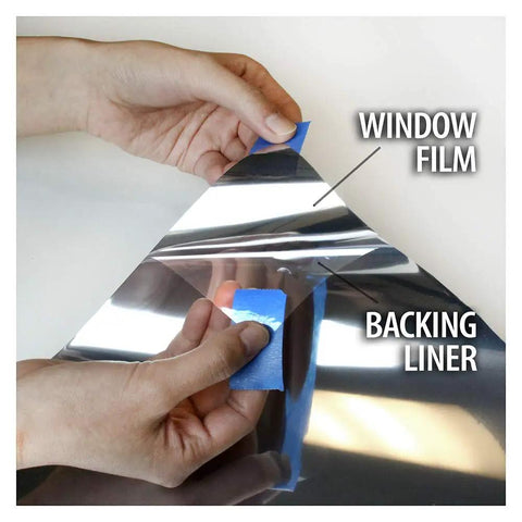 Hands peeling Very Dark Daytime Privacy Window Film With Heat Control Mirror Silver Tint Extra Reflective Silver Shade 36 Inch by 12 Foot Roll from backing liner.