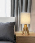 Set Of 2 Wood Tripod Bedside Lamps With Linen Fabric Shade illuminating a bedroom on a wooden nightstand.