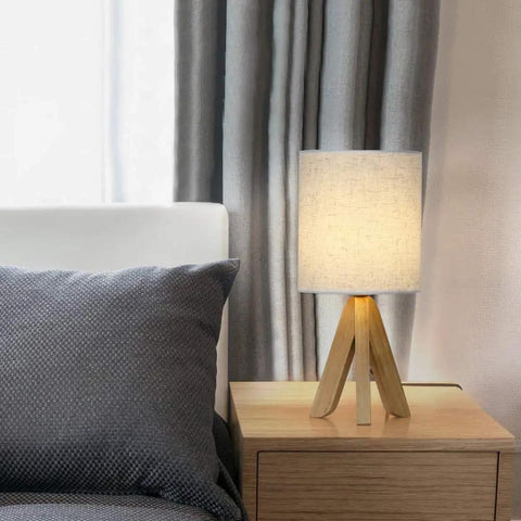 Set Of 2 Wood Tripod Bedside Lamps With Linen Fabric Shade illuminating a bedroom on a wooden nightstand.