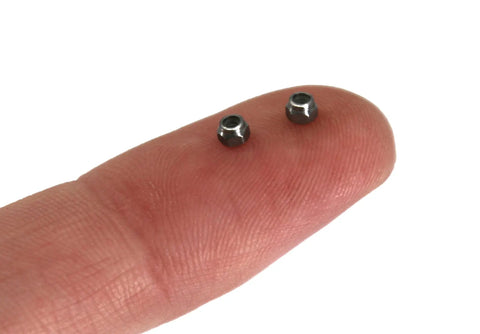 Close-up of two Stainless Steel Fingerboard Lock Nuts With Nylon Inserts Pack Of Six on a fingertip, pro-grade hardware.