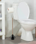 Heavy Duty Rubber Toilet Plunger With Solid Wooden Handle For Bathroom Sink Drains And Tub Clogs standing next to a toilet.
