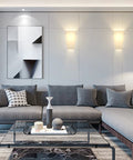 Modern living room with Dope Wall Sconces Set Of Two, acrylic shades, mounted on a wall above a grey sectional sofa with decorative cushions.