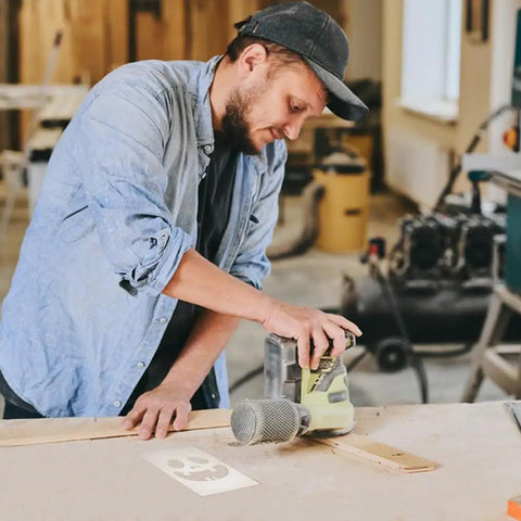 Man using router on wood with Halloween skull template, focusing on detailed carving for his DIY craft project.
