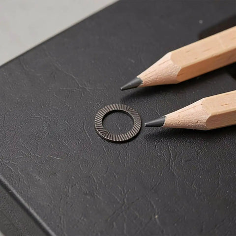 72 Piece Set Double Tooth Lock Washers Black Ironclad Grip 65mn Steel on a black surface with pencils for scale.