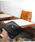 Dang Solid Table Leg Brackets Featuring Heavy Duty Mounting Plates For Sofa Couch And Chair Repair Easy As Pie Installation Home Fix Kit That Never Lets Down in a hand with a background of wooden tables and chairs.