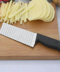 Top view of stainless steel crinkle-cut potato knife with black handle on cutting board