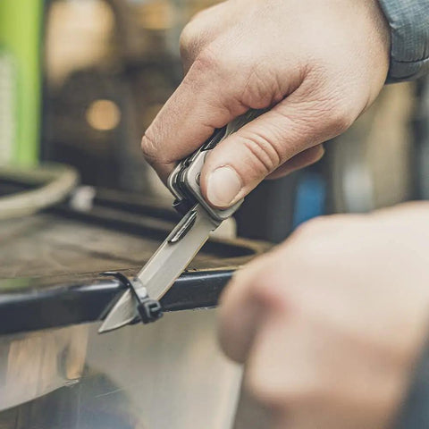 Person using Lockdown Driver 7 In 1 EDC Multitool With A 2.5 Inch Plain Edge Blade to cut a zip tie on a container, showcasing its practicality.