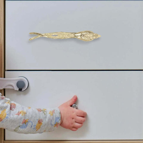 Dope Brass Bird Shape Cabinet Handles With Golden Finish installed on white drawer, featuring sleek design, child hand visible