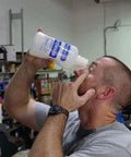 PhysiciansCare eyewash bottle, 32 oz, side view, being poured into eye by man in a workshop