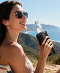 Person holding a 3 In 1 Slim Can Cooler For 12 Oz Skinny Cans Regular Cans And Beer Bottles Keeps Drinks Cold Up To 6 Hours With Double Walled Stainless Steel Vacuum Insulation No Sweat Matte Black Finish by the sea