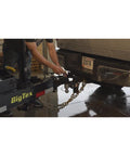 Person attaching 3/8 Inch Grade 70 Agricultural Safety Chain With Clevis Grab Hook And Attachment Ring, 5 Feet Long, 6600 Lb Load Capacity For Farming, Logging, And Construction Towed Machines to a trailer hitch.