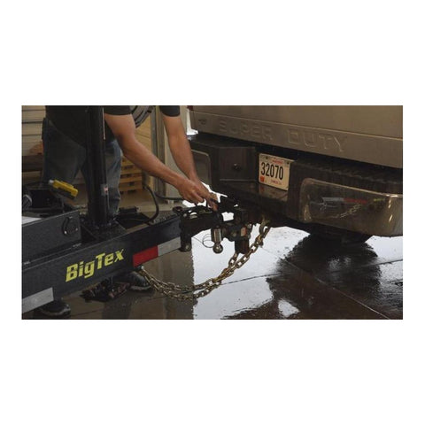 Person attaching 3/8 Inch Grade 70 Agricultural Safety Chain With Clevis Grab Hook And Attachment Ring, 5 Feet Long, 6600 Lb Load Capacity For Farming, Logging, And Construction Towed Machines to a trailer hitch.
