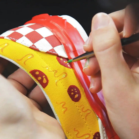 Close-up of applying White Acrylic Leather Paint 1 Fl Oz Flexible Crack Scratch Peel Resistant to a sneaker with colorful designs.