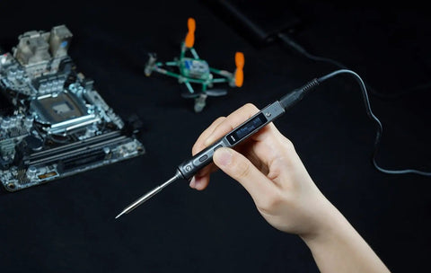Hand holding Ts101 Portable Soldering Iron With PD And DC Dual Power, 50-400 C Adjustable, near circuit board and drone
