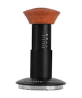 Heavy Hitter Spring Loaded Coffee Tamper With Precision Distribution Leveler And Clear Pressure Scale For Flawless Espresso Pucks on a white background, featuring a hardwood handle and measuring scale.