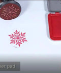 Engraving rubber stamp with red snowflake design pressed onto white paper; red ink pad case visible nearby.