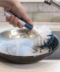 Heavy Duty Sink And Dish Scrub Brush With Safe Bristles cleaning a soapy skillet at the sink, designed for tough food residue.