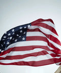 Hands holding 2x3 Indoor Outdoor US Flag Made From Polyester Nylon With Double Stitch Edges And Brass Grommets, waving in breeze.