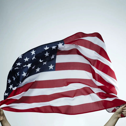 Hands holding 2x3 Indoor Outdoor US Flag Made From Polyester Nylon With Double Stitch Edges And Brass Grommets, waving in breeze.