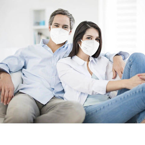 Couple wearing KN95 Face Masks 50 Pack Individually Wrapped White 5 Layer Protection Cup Style For Adults Men Women Indoor Outdoor Use Dust Safety Mask Great For Travel On The Go And Everyday Errands, sitting on sofa.
