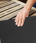 Get The Ultimate Multipurpose Sandpaper Set With 10 Sheets Of Assorted Grits with a hand smoothing grey sandpaper on a wooden table.