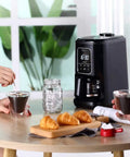 Compact Automatic Freshly Ground Coffee Brewer With Onboard Bean Grinder And Programmed Cup Settings in use with coffee and pastries.