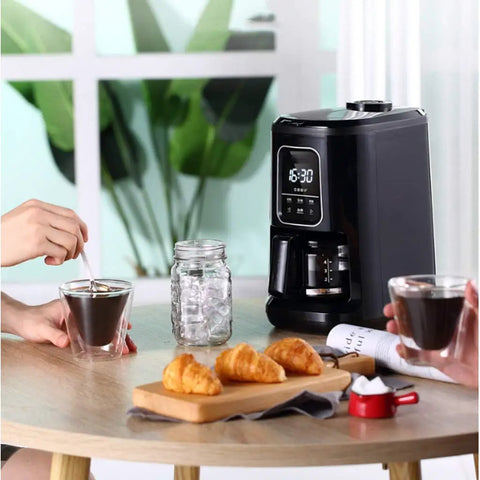 Compact Automatic Freshly Ground Coffee Brewer With Onboard Bean Grinder And Programmed Cup Settings in use with coffee and pastries.