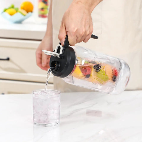 Fruit Infuser Glass Water Pitcher With Wide Mouth 2 Quart Leakproof No Spill Mason Style Jar Filter Lid For Easy Infused Water Durable Glass For Home Kitchen Bar Or Picnic Easy Pour And Clean in use, pouring infused water into a glass on a kitchen counter.