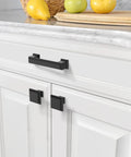 10 Pack 1.3 Inch 32mm Matte Black Cabinet Knobs on white kitchen cabinets next to fruit basket and cutting board
