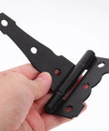Hand holding 4 Inch T Shaped Barn Door Hinge Set Black Iron Heavy Duty Gate Hardware For Doors And Windows Matte Finish Provides Sturdy Support And Stability For Indoor Shed Barn And Exterior Use 2 Pcs against white background