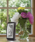 Slick Digital Thermometer With Indoor And Outdoor Temperature Readouts next to a vase of flowers on a windowsill.