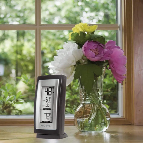 Slick Digital Thermometer With Indoor And Outdoor Temperature Readouts next to a vase of flowers on a windowsill.