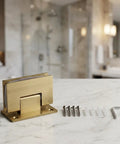 Glass Door Hinges For Shower And Office Partitions With A Smooth 180 Degree Swing And Stable Panels, Heavy Duty Rust Resistant 304 Stainless Steel For Bathrooms, Laundry Rooms, And Humid Spaces. Brushed gold hinge with screws on marble surface